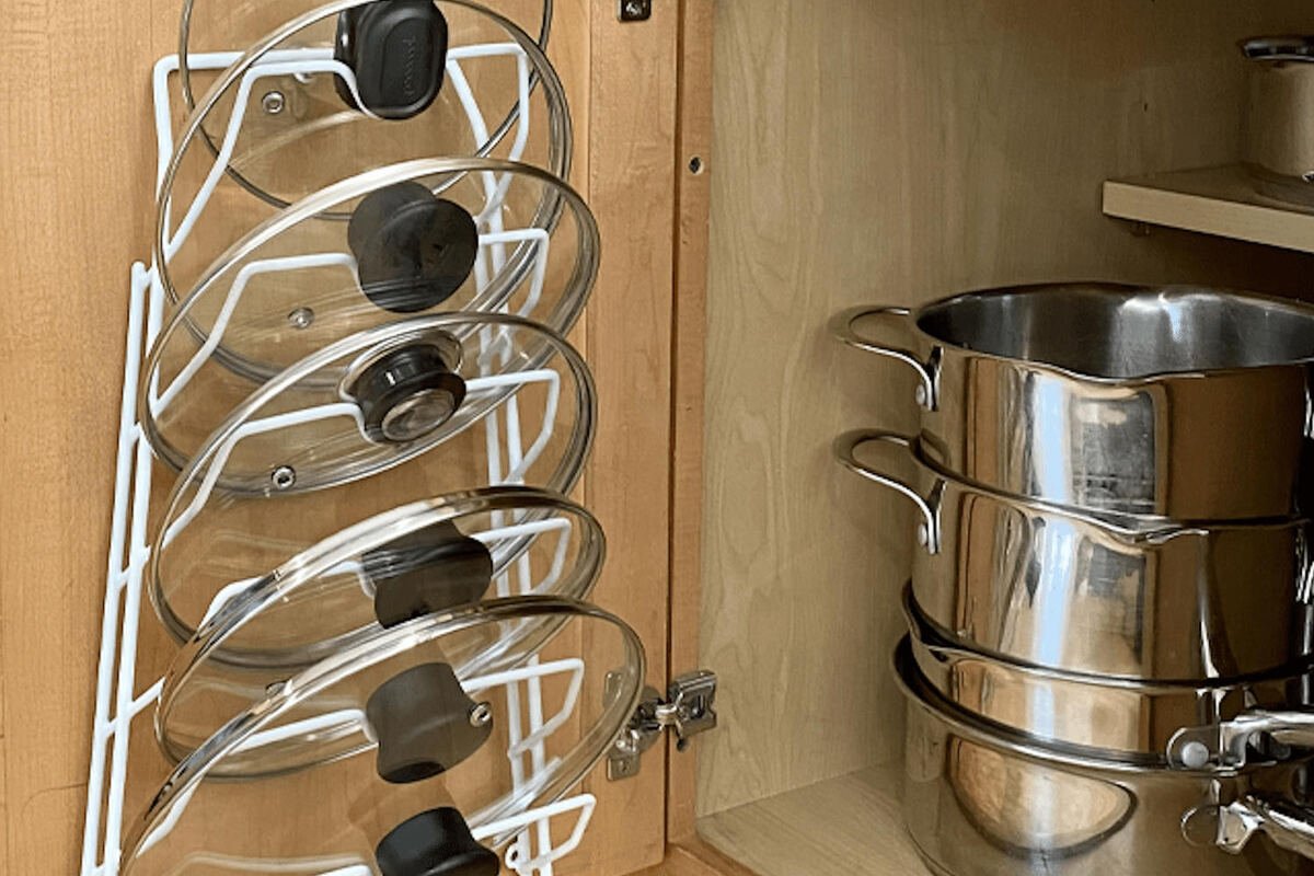Pot lids standing upright in a rack inside a kitchen cupboard